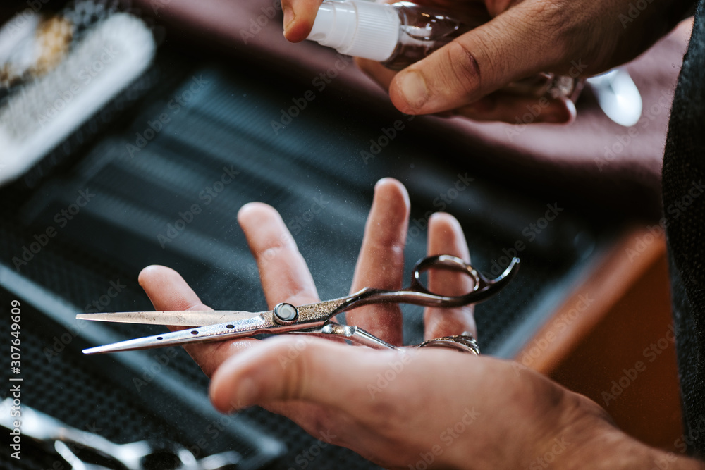 cropped view of barber holding antibacterial spray near scissors