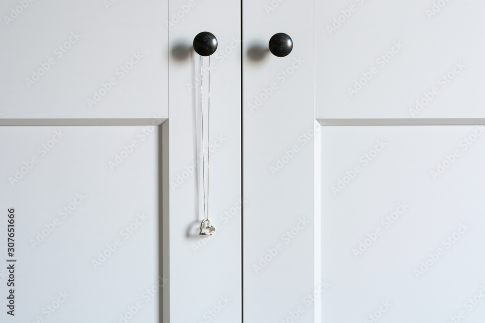 White wardrobe doors with a hanging necklace with silver heart pendant. Minimalistic style. White wardrobe doors with a hanging necklace with silver heart pendant. Minimalistic style.