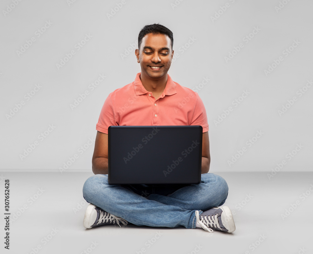 technology, internet, communication and people concept - happy indian man with laptop computer sitting on floor over grey background technology, internet, communication and people concept - happy indian man with laptop computer sitting on floor over grey background