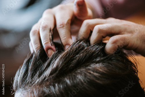 Vászonkép cropped view of barber with black hair pomade on hands styling hair of man in ba