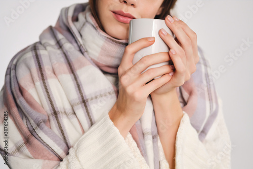 Close up attractive girl with scarf holding cup with warm drink near face over white background