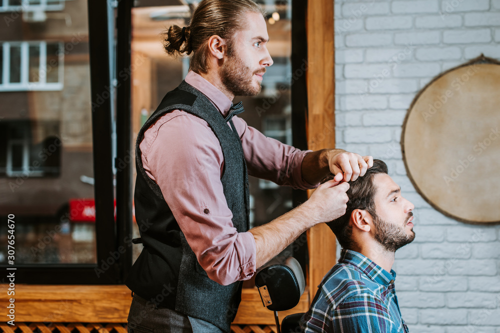 side view of barber styling hair on cheerful bearded man