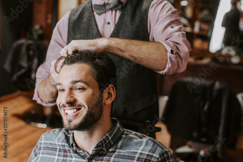 barber styling hair on cheerful bearded man