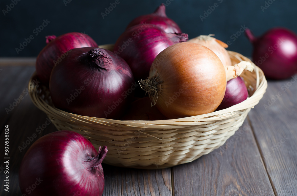 Red onions in a wicker basket. Brown wooden background.