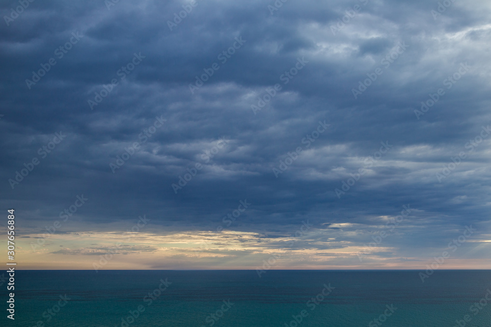 Dark dramatic cloudscape over blue sea water. Heavy clouds of thunderstorm. Horisontal color photography.