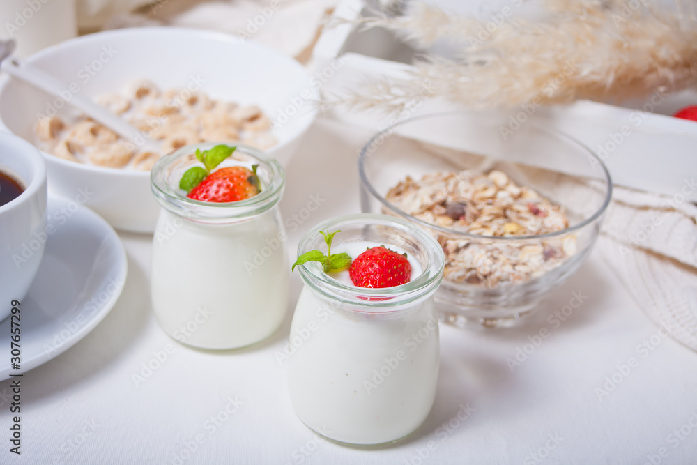 Two portions natural homemade yogurt in a glass jar with fresh strawberry and muesli nearby Two portions natural homemade yogurt in a glass jar with fresh strawberry and muesli nearby