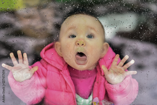 Baby trying to lick rain drops on the window's glass outside, pressing face against the glass