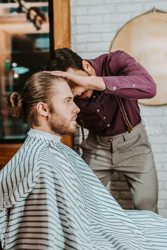 barber styling hair of bearded man in barbershop