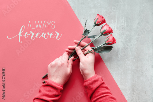 Flat lay with two female hands holding red roses on diagonal paper background on stone. Text 