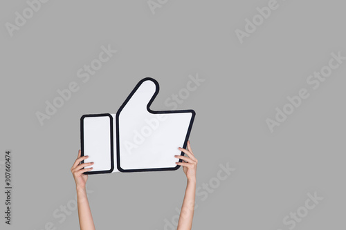 Hands holding the sign of like on grey studio background. Negative space to insert your text or image, advertising. Social media, showing meaning, communication, gadgets, modern technologies. photo