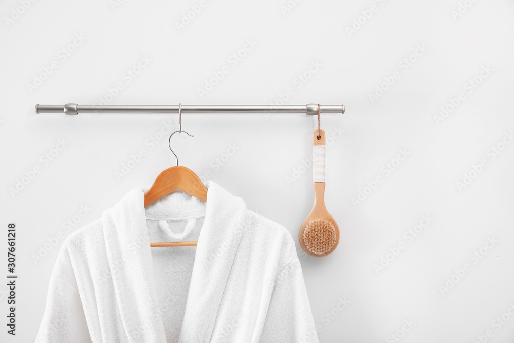 Hanger with clean bathrobe and brush on light wall - obrazy, fototapety, plakaty 