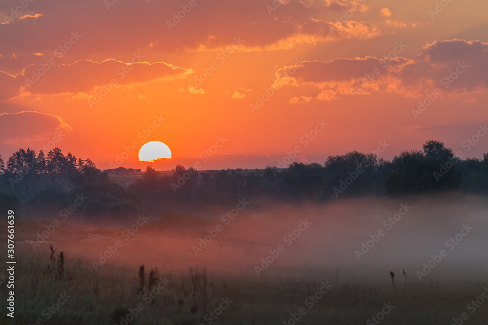 Obraz premium Sunrise through the clouds. Fog creeps across the meadow.