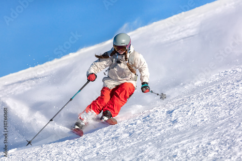 Girl On the Ski. a skier in a bright suit and outfit with long pigtails on her head rides on the track with swirls of fresh snow. Active winter holidays, skiing downhill in sunny day. Dynamic picture