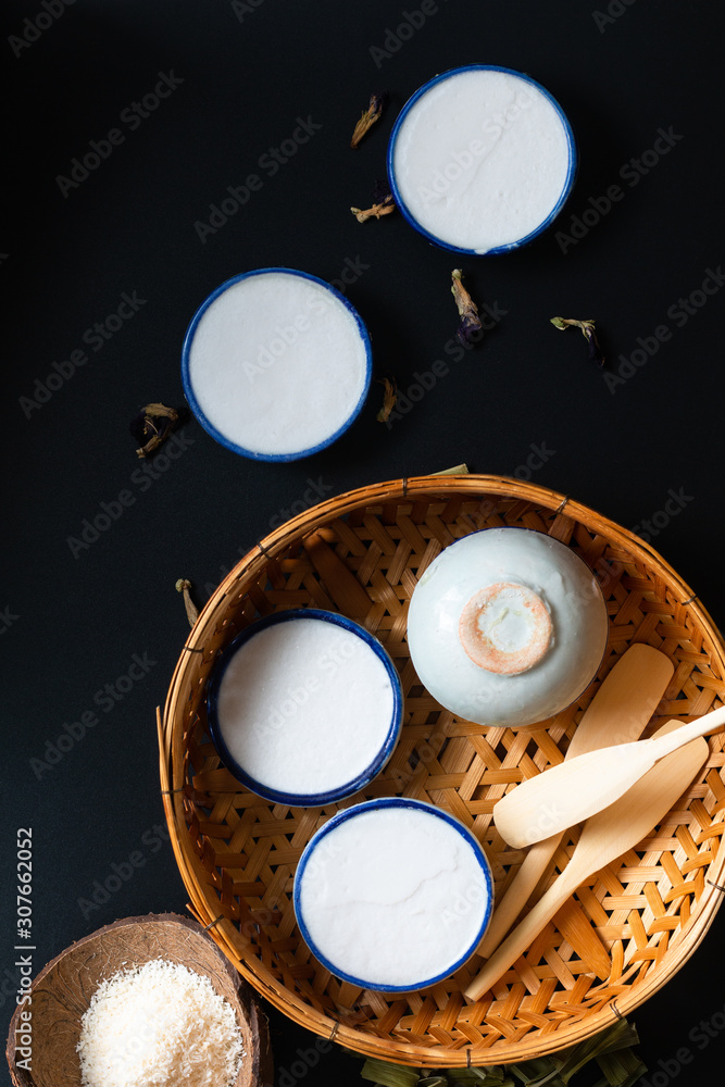 Food dessert concept Thai dessert Kanom Tuay Coconut Rice and pandan Custard in small porcelain cup and bamboo bastket on black background with copy space Food dessert concept Thai dessert Kanom Tuay Coconut Rice and pandan Custard in small porcelain cup and bamboo bastket on black background with copy space