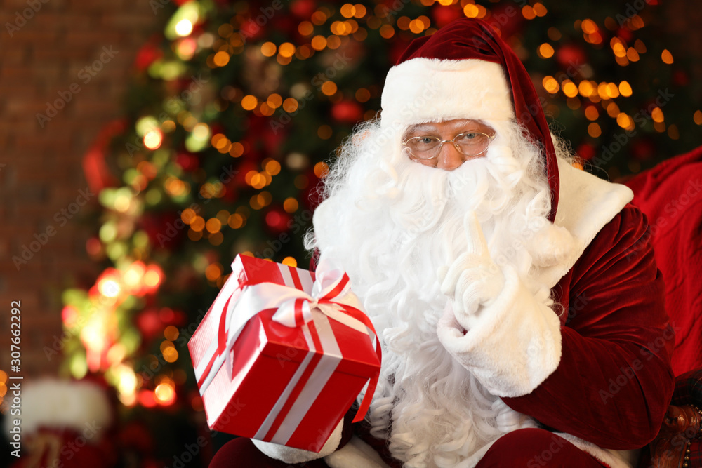 Santa Claus with gift box near Christmas tree indoors Santa Claus with gift box near Christmas tree indoors