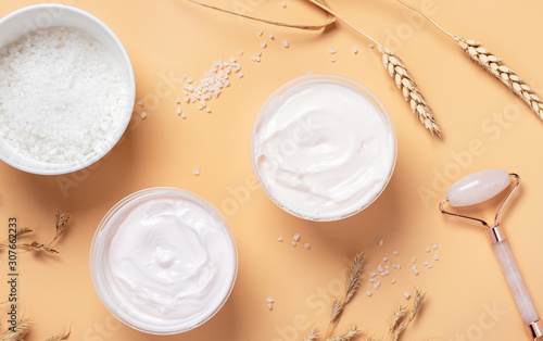 White cream, salt in the bowl, gua sha roller, spikelets of wheat and oats on a beige background, top view. Body and skin care at home concept. Ingredients for scrub with salt flat lay.