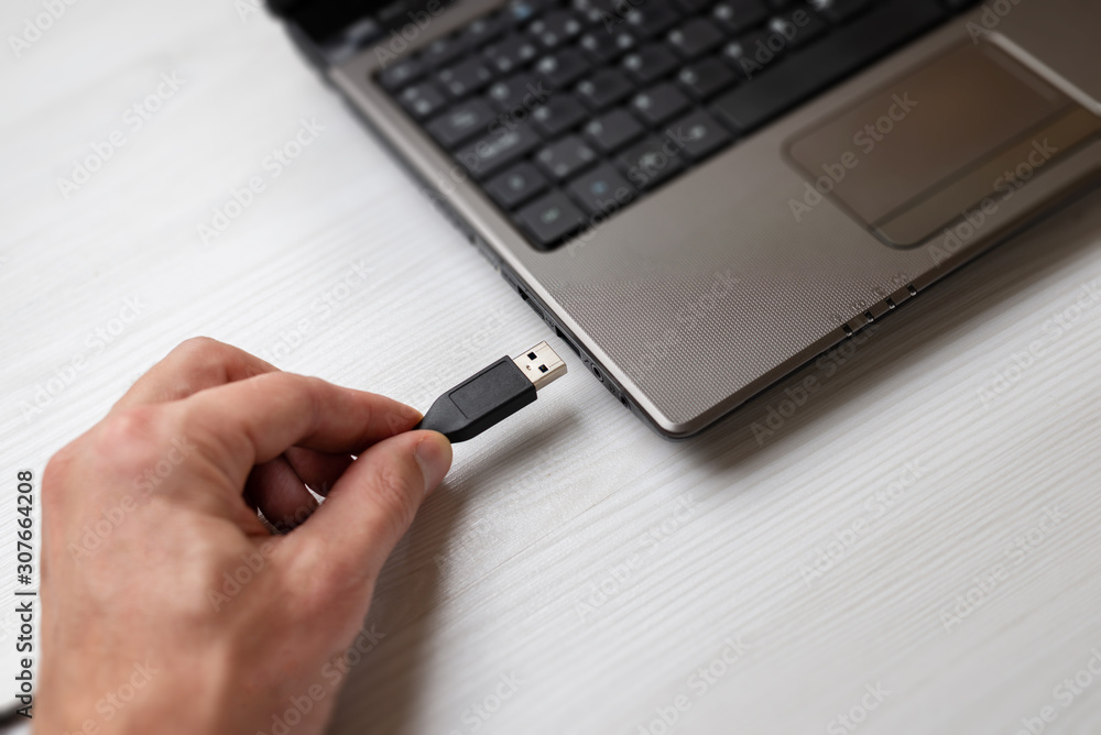 Fototapeta premium Hand holding usb cable and plugs it into the usb port on the laptop computer close-up
