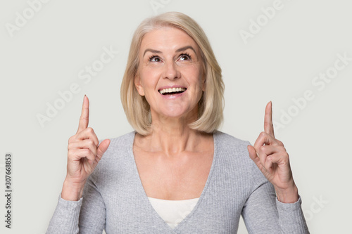 Fotografi Happy mature woman look up showing up with fingers portrait