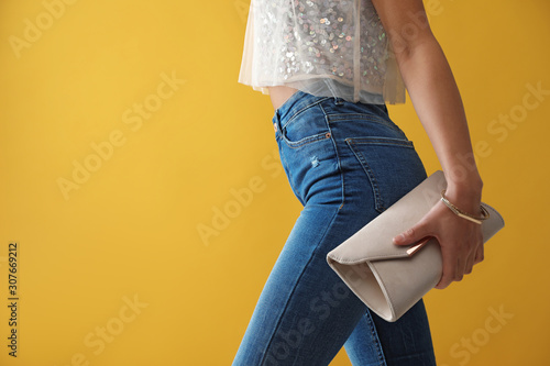 Woman in jeans with clutch purse on yellow background, closeup. Space for text