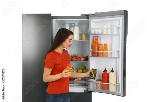 Young woman choosing products from refrigerator on white background
