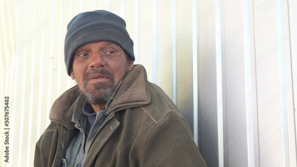 Homeless man during conversation outdoors. Beggar sitting on the street near the fence. Homeless man during conversation outdoors. Beggar sitting on the street near the fence.