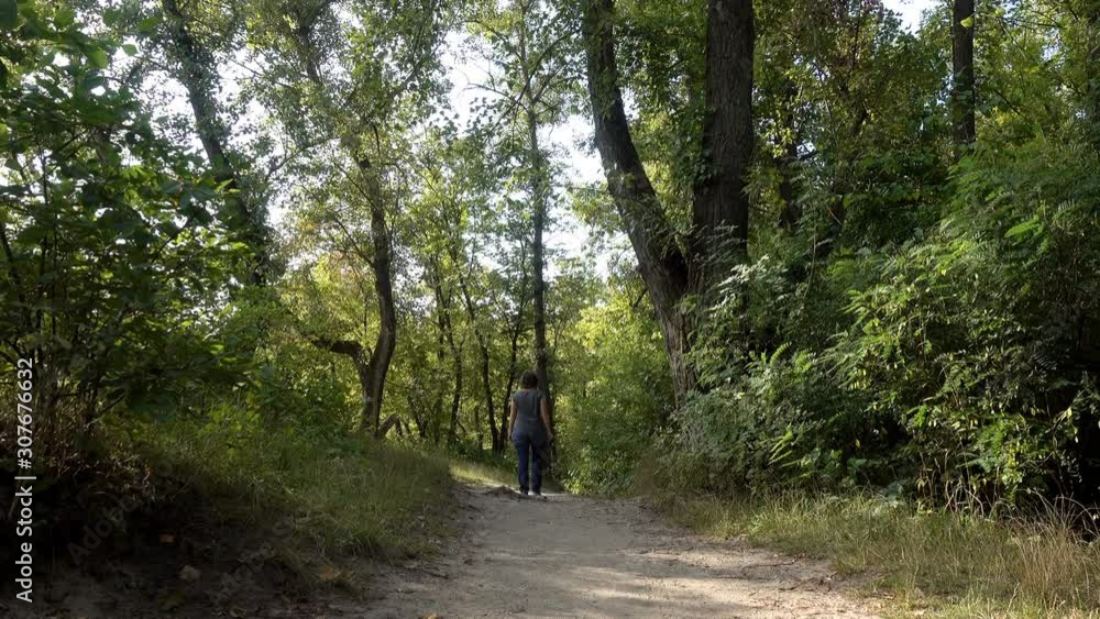 4K view of a woman walking along a path among green trees and bushes. Woman moves deep into the forest 4K view of a woman walking along a path among green trees and bushes. Woman moves deep into the forest