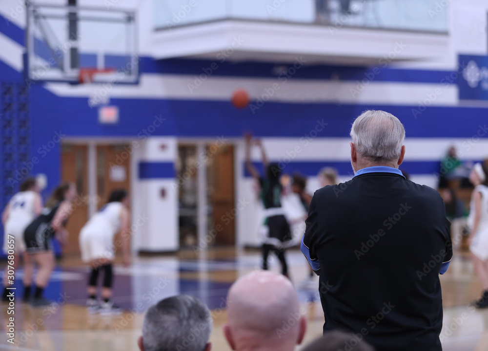 A basketball coach watches an opposing player shoot a foul shot