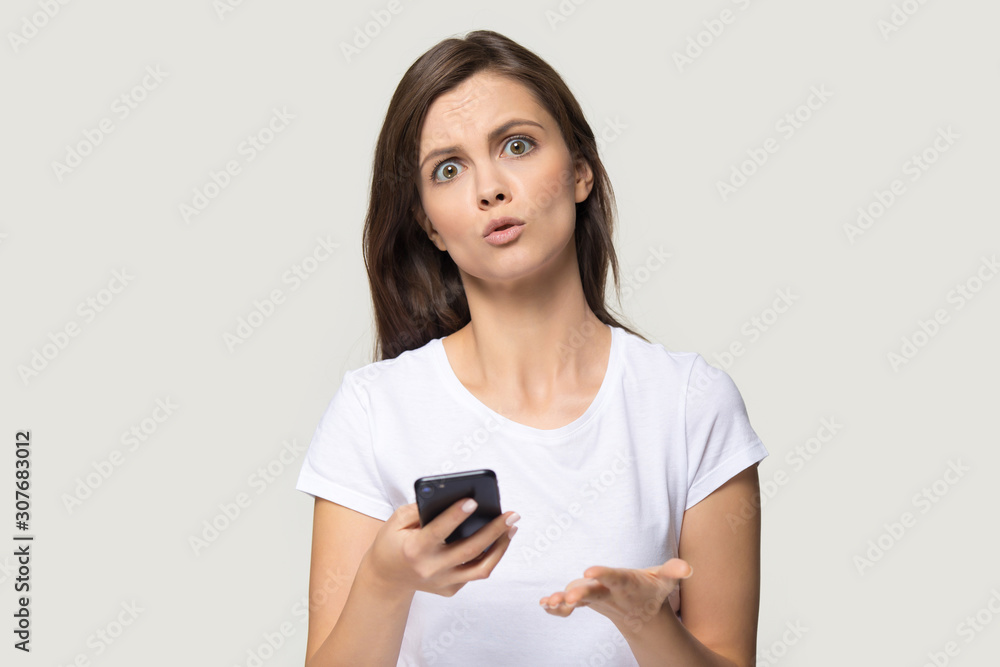 Headshot of confused woman holding phone with unhappy face Headshot of confused woman holding phone with unhappy face