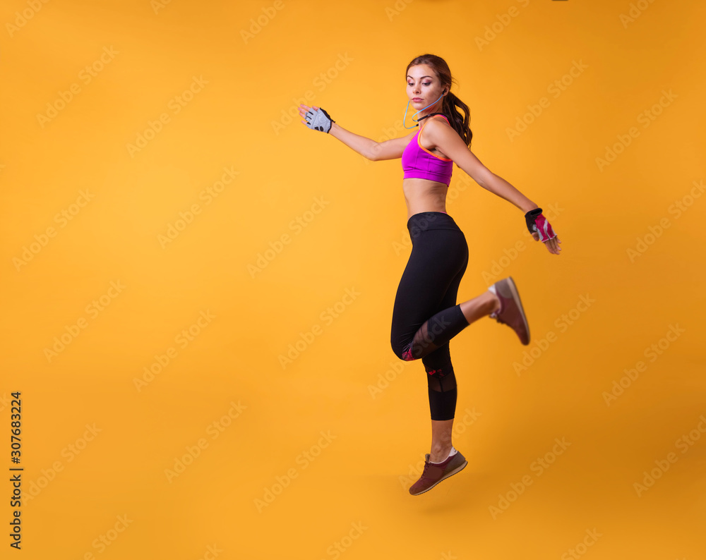 Inspired woman training in headphones. Slim caucasian girl doing excersizes.Woman in sportswear running over yellowbackground. Full length shot of healthy young caucasian woman sprinting. Copy space.