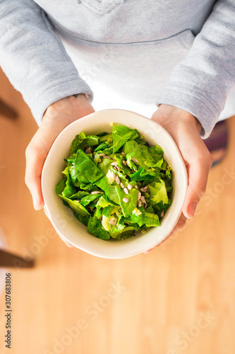 Woman hands holds green salad with spinach.