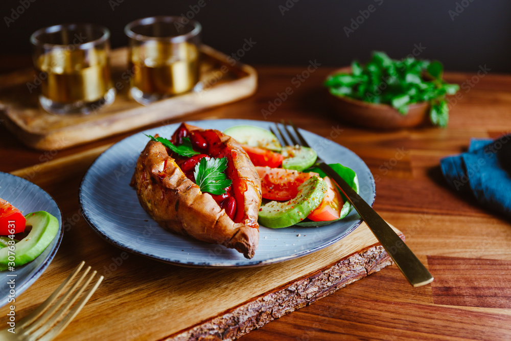 Baked sweet potato filled with red beans stewed in tomato paste served with avocado and cherry tomatoes on a plate. Healthy veggie recipe. Baked sweet potato filled with red beans stewed in tomato paste served with avocado and cherry tomatoes on a plate. Healthy veggie recipe.