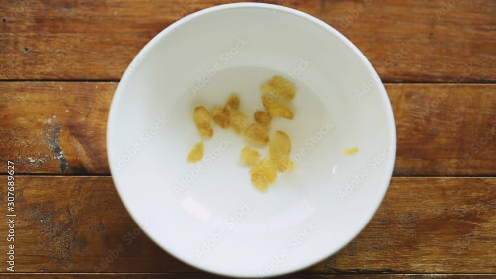 Slow motion food breakfast pouring corn flake cereal into the white bowl in wood background