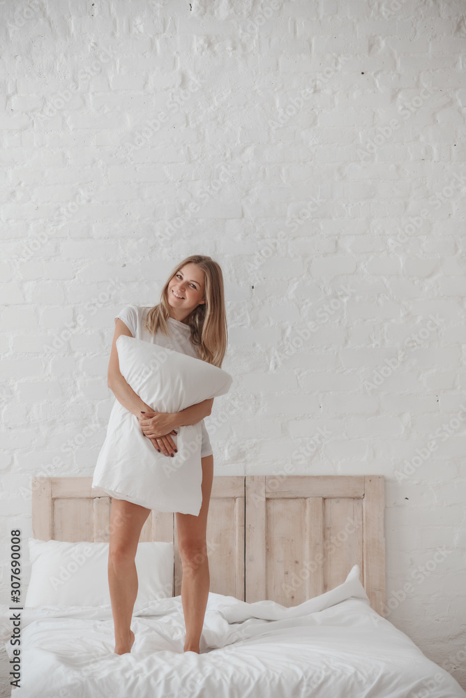 Attractive girl with long blonde hair in white t-shirt hugging with pillow Attractive girl with long blonde hair in white t-shirt hugging with pillow