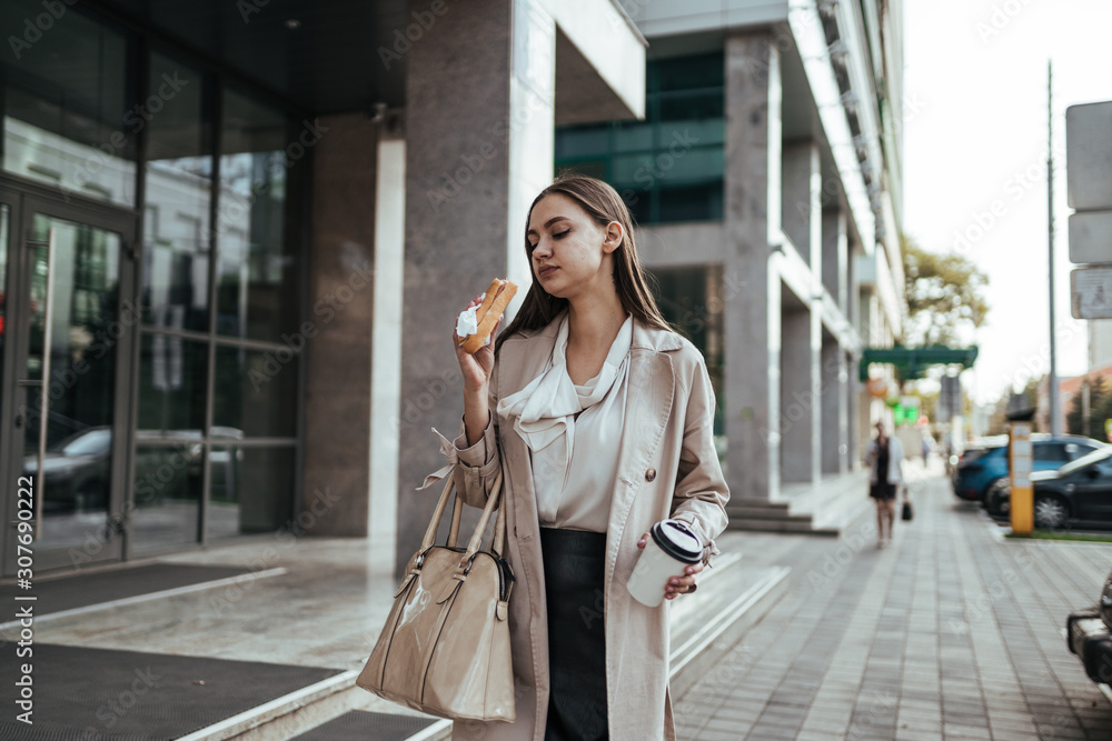 Fototapeta premium girl chewing a pie walks down the street of the business center