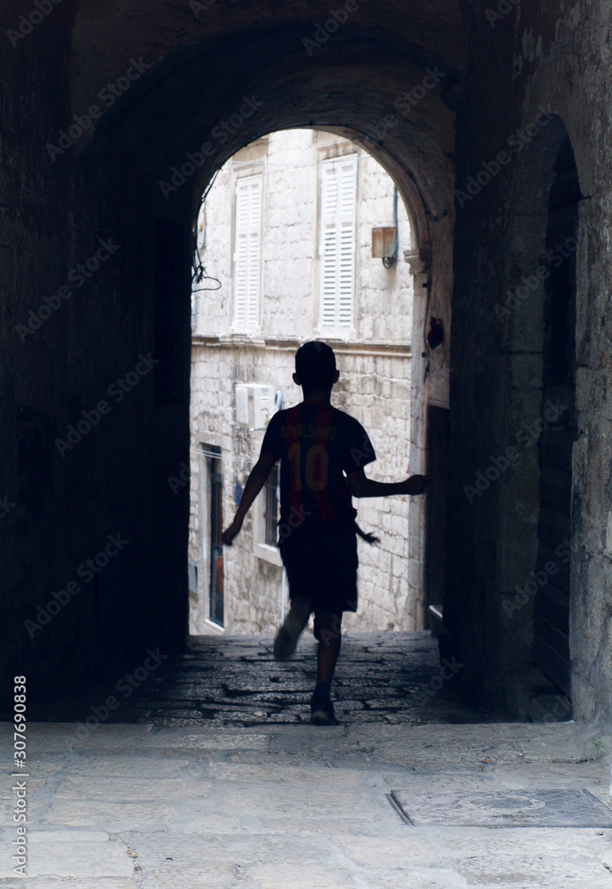 an atmospheric alleyway with a silhouette of a boy running through having fun in an ancient city in europe. young generation in an old environment. youth playing in an urban setting.