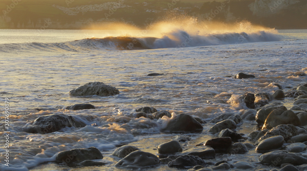 Obraz premium Spray above crest of breaking wave backlit by sunlight