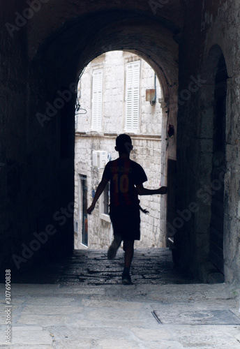 an atmospheric alleyway with a silhouette of a boy running through having fun in an ancient city in europe. young generation in an old environment. youth playing in an urban setting.