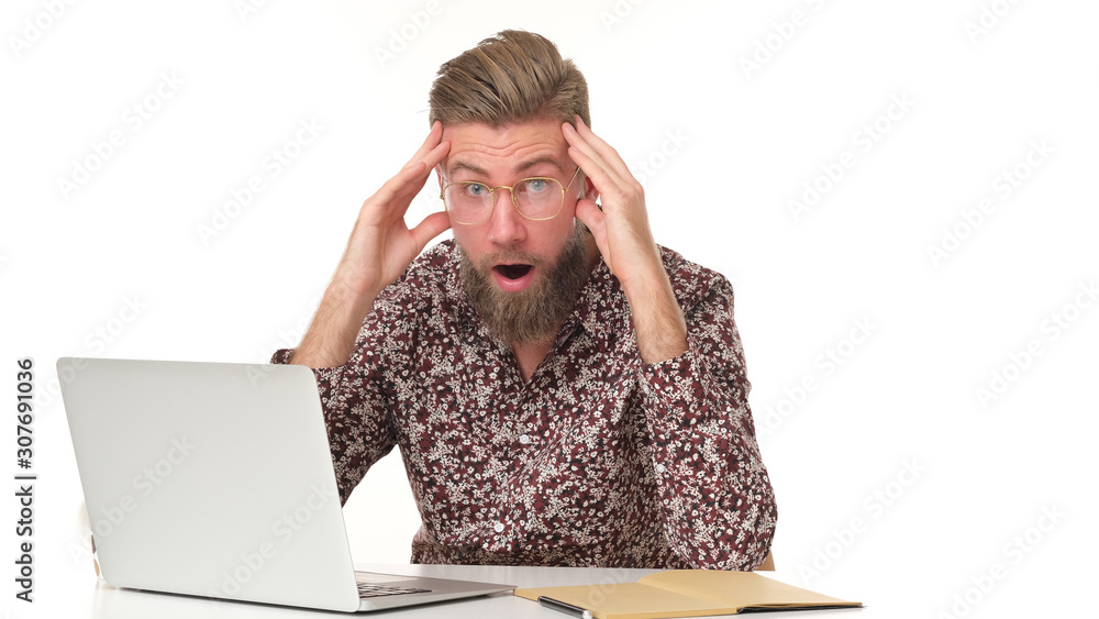 Man with beard in flowery pattern shirt can't believe whats happening sitting in front of computer. Man with beard in flowery pattern shirt can't believe whats happening sitting in front of computer.