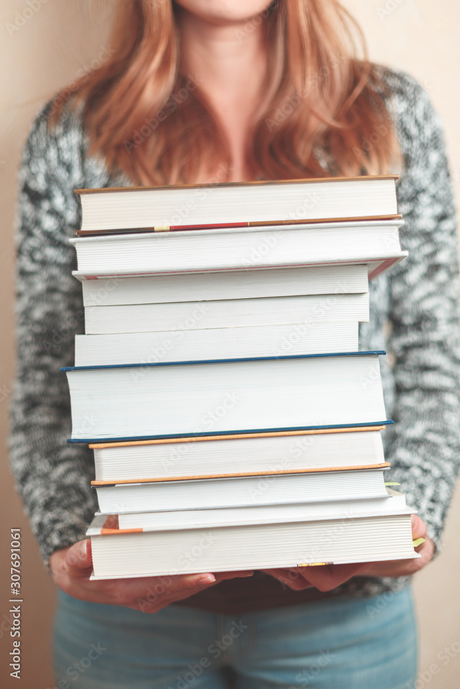 A stack of books is held by a woman. Books are in focus. The background is blurry. A stack of books is held by a woman. Books are in focus. The background is blurry.