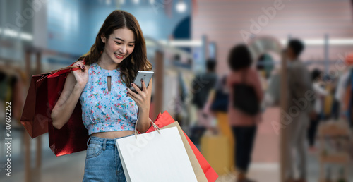 Shopping woman holding shopping bags looking on smartphone in shopping mall background.