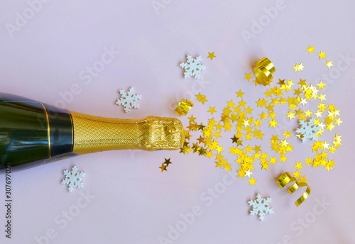 a bottle of champagne on a pink background with a scattering of confetti in the form of gold stars and white snowflakes, with space. For text, flat lay