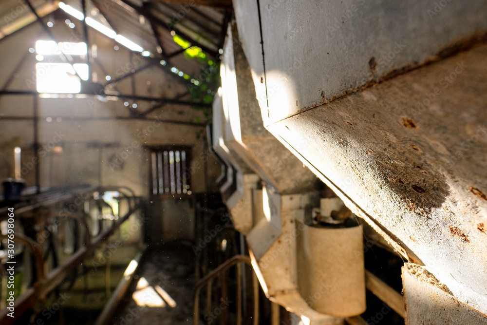 Shallow focus on a grain hopper seen inside a now derelict milking parlour in dairy farm,Sun light is seen entering an opening, showing up dust particles in the sunlight.