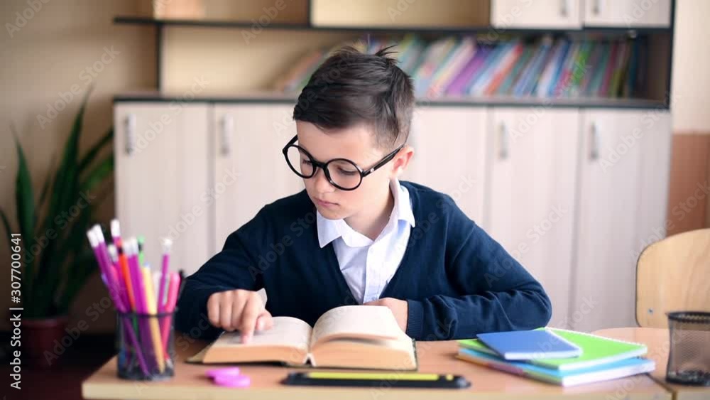 Funny schoolboy with glass in uniform reading a textbook in classroom Funny schoolboy with glass in uniform reading a textbook in classroom