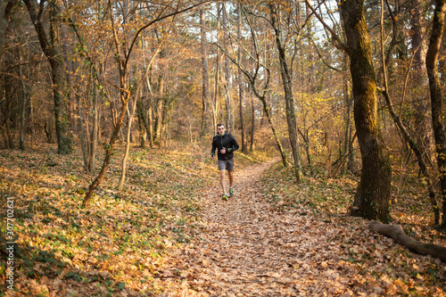 The concept of sport and a healthy lifestyle. A young slender man in sports clothes is engaged in Jogging in the autumn forest or Park. The view from the front
