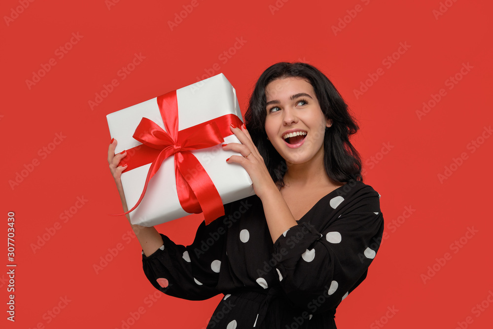 Brunette woman in a black dress smiling holding Christmas giftbox of white color with red ribbon. Brunette woman in a black dress smiling holding Christmas giftbox of white color with red ribbon.