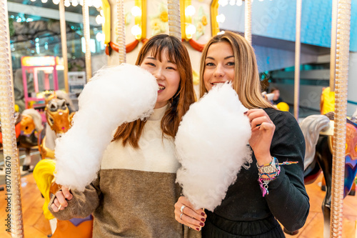 couple of young multi-ethnic women eating cheerful cotton candy at a party.