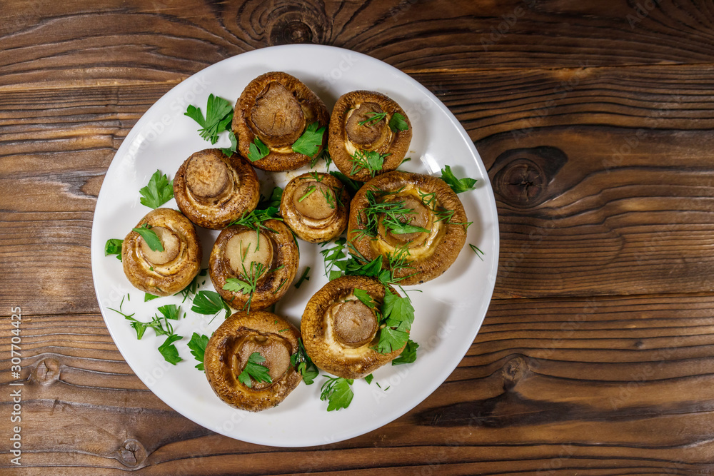 Baked mushrooms in plate on wooden table. Top view Baked mushrooms in plate on wooden table. Top view