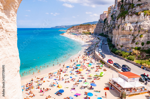 Rotonda beach full of people. Amazing Italian beaches. Sea promenade scenery in Tropea with high cliffs with built on top city buildings and apartments.