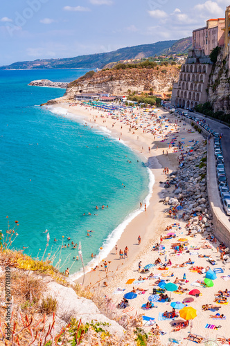 Rotonda beach full of people. Amazing Italian beaches. Sea promenade scenery in Tropea with high cliffs with built on top city buildings and apartments.