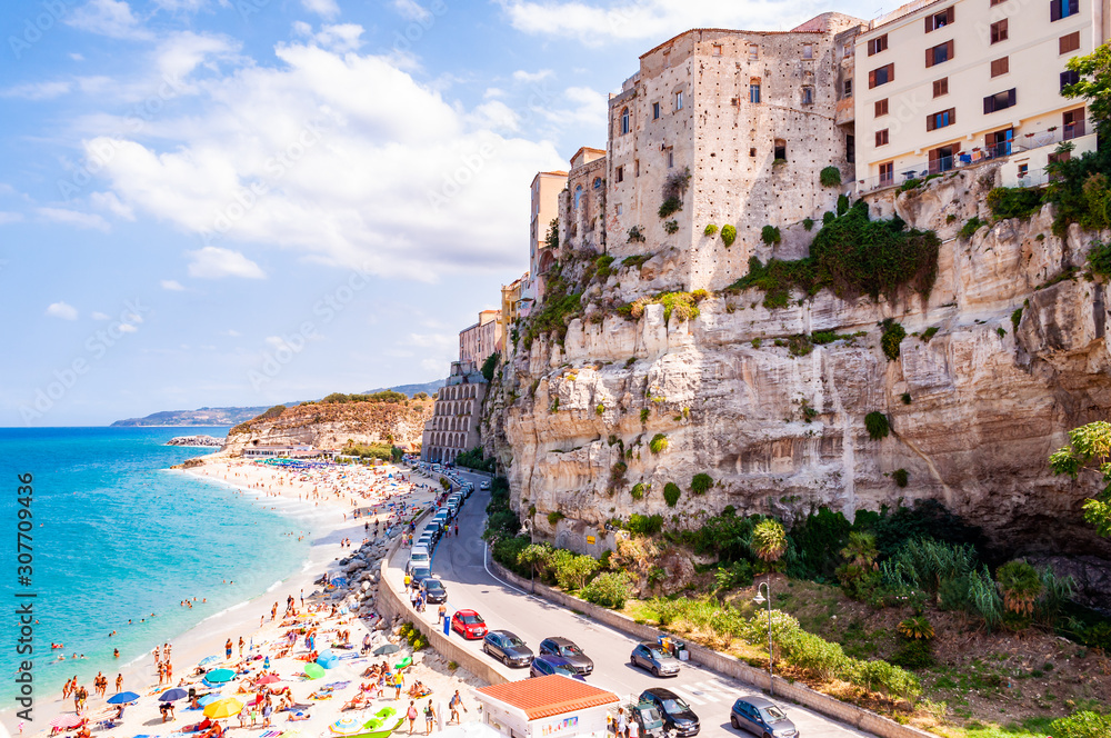 Sea promenade scenery in Tropea with high cliffs with built on top city buildings and apartments. Rotonda beach full of people. Amazing Italian cityscape